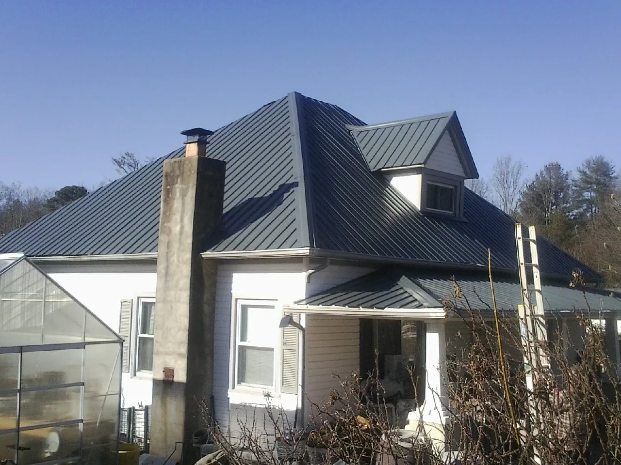 Dark blue standing seam metal roof on a white farmhouse with dormer — Slate & Tile Roof Repair by Roofing Brothers in Guffey