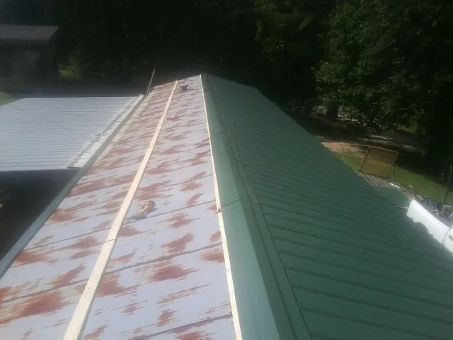 Old rusted panels beside newly installed green metal roofing — Wind Damage Roof Repair by Roofing Brothers in Guffey