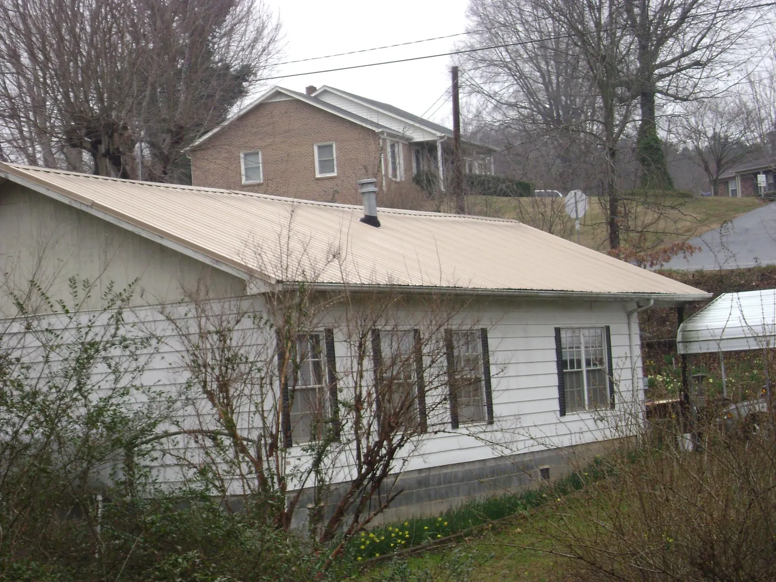 Tan metal roof on a white sided house set into a hillside — Commercial Roofing by Roofing Brothers in Guffey