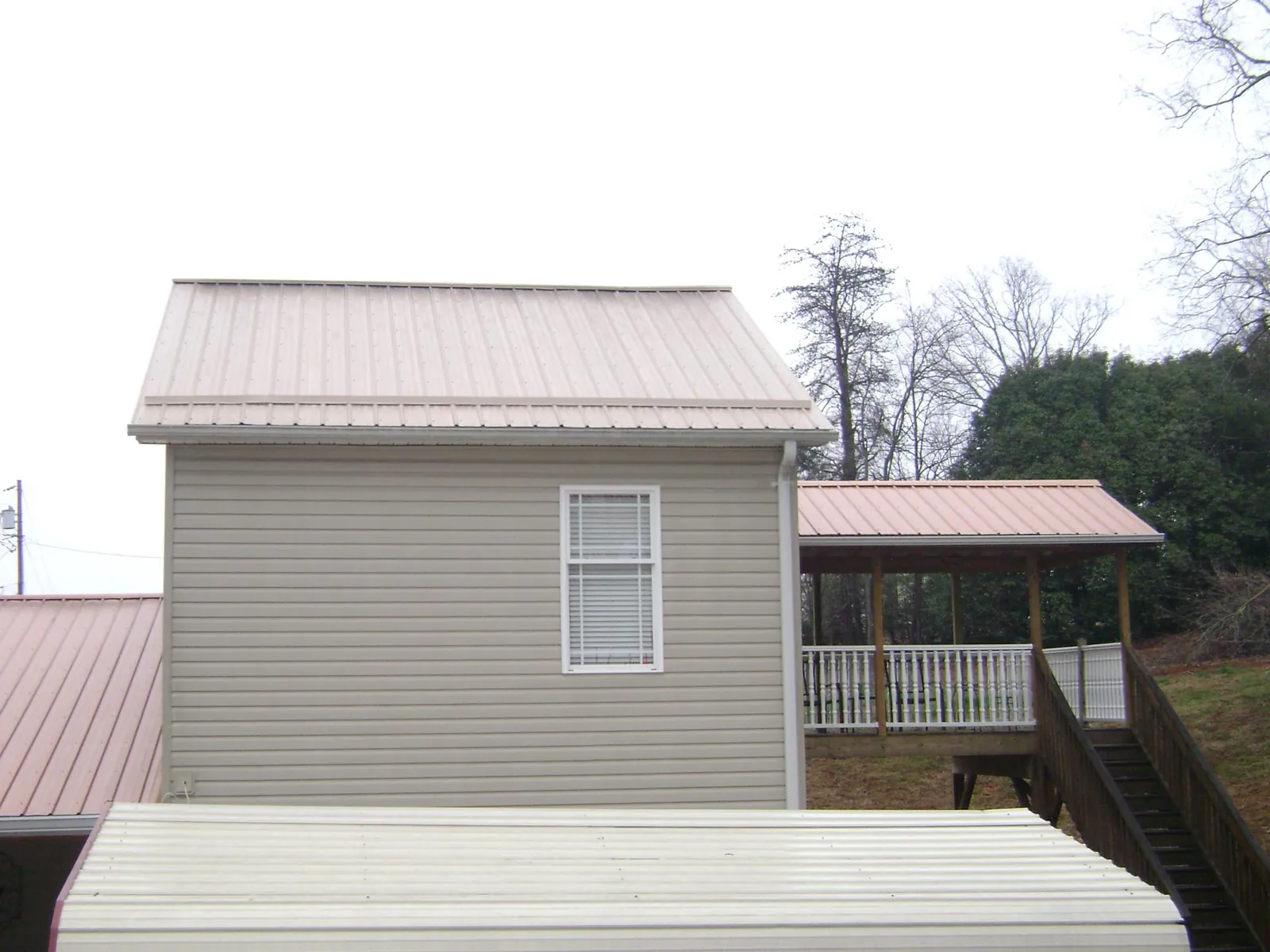 Tan metal roofs on a two story addition and attached porch, from a Roof Replacement job in Guffey